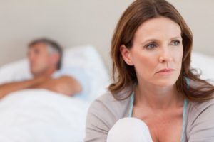 11685180 - sad mature woman on bed with her husband in the background